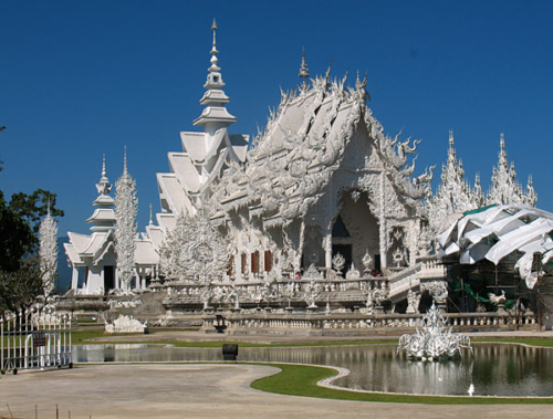 Wat Rong Khun, perhaps better known to foreigners as the White Temple, is a privately owned art exhibit in the style of a Buddhist temple in Chiang Rai Province, Thailand. It is owned by Chalermchai Kositpipat, who designed, constructed, and opened it to visitors in 1997.